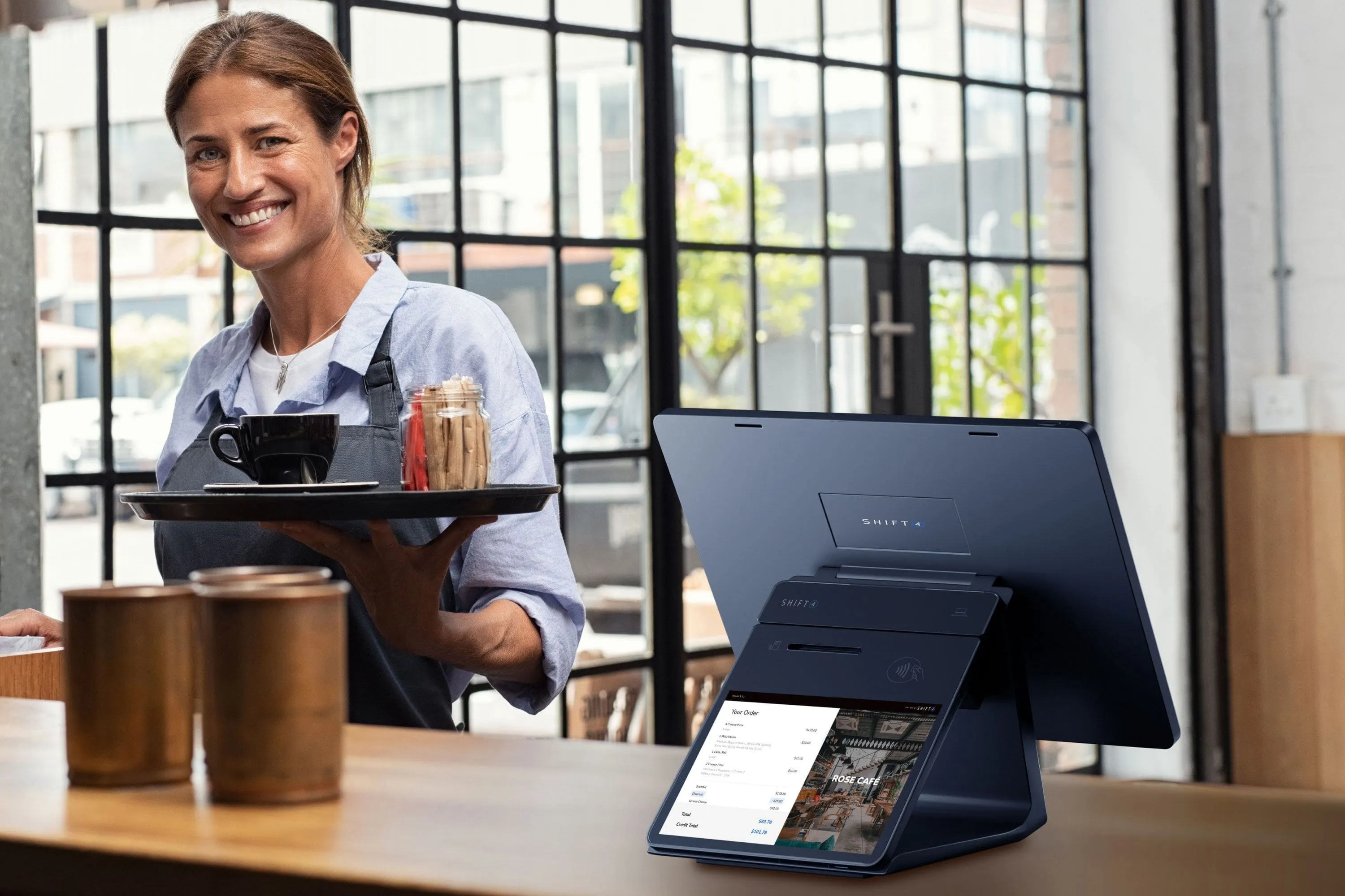Server carrying a tray past a SkyTab customer facing display on a cafe counter