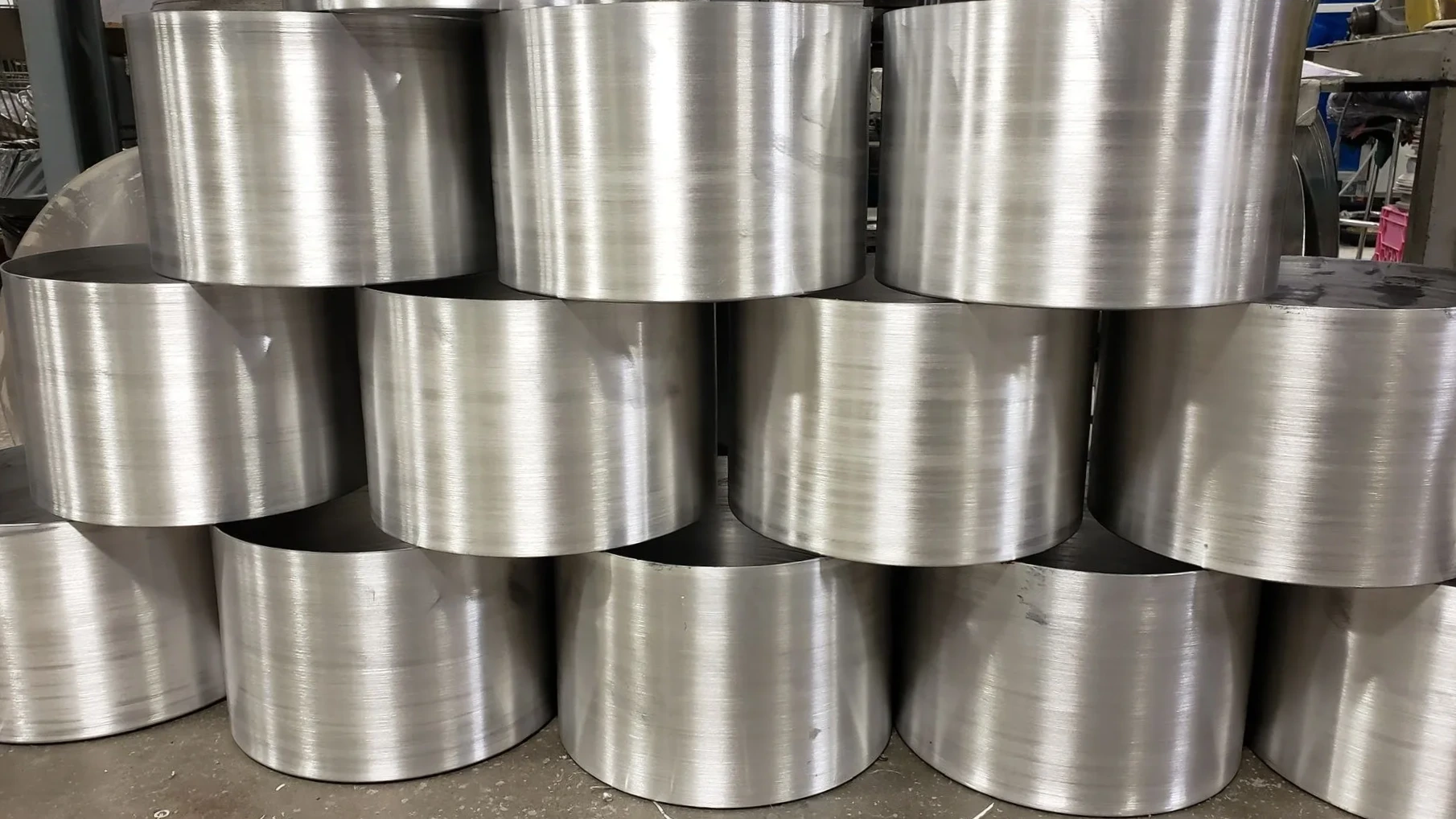 Stacked short cylindrical metal pieces with a shiny brushed finish, arranged in a grid formation on a workshop floor.
