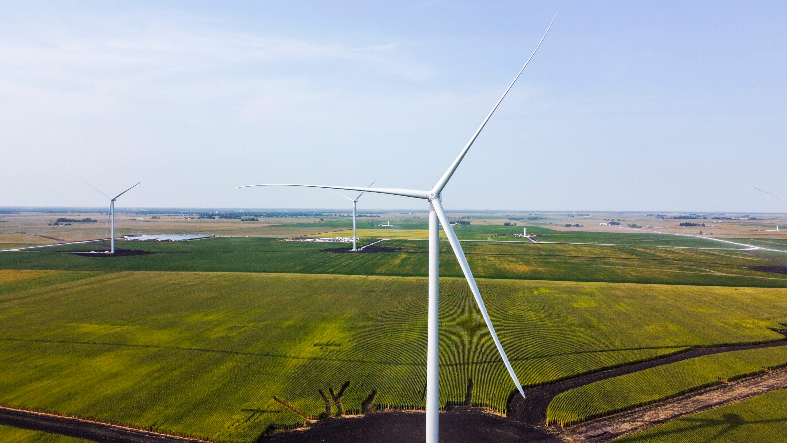 Aerial view of several large white wind turbines in green farmland under a clear sky.