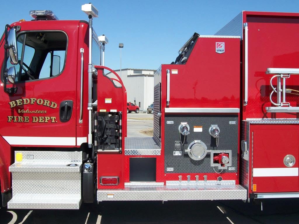 Close-up of red Bedford Volunteer Fire Dept. fire truck showing side compartments and water controls.
