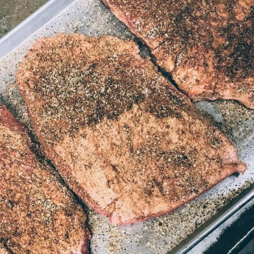 Raw pork chops seasoned with black pepper and spices on a baking tray ready to be cooked.