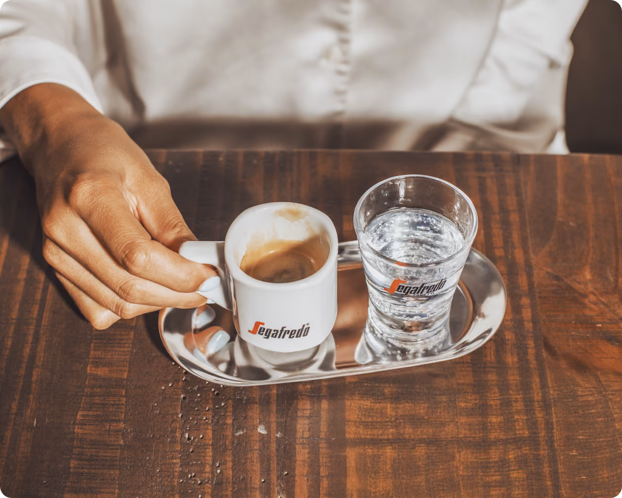 A hand setting down a Segafredo espresso cup beside a glass of water