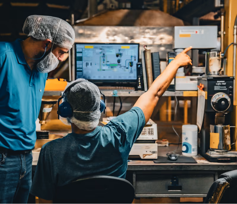 Two production employees in hairnets monitoring a roast profile on a control room screen