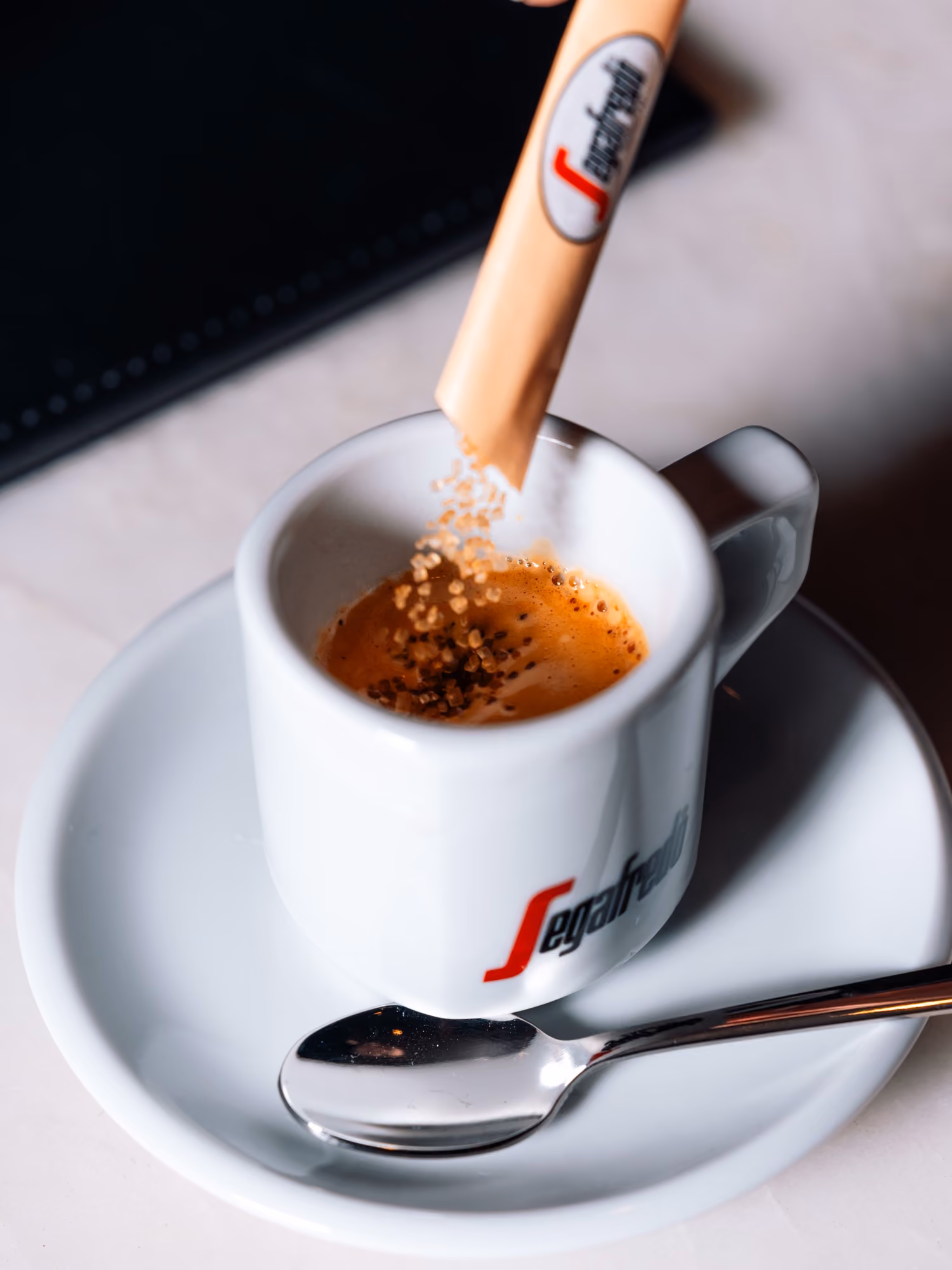 A Segafredo espresso finished with sugar, served on a saucer with a spoon
