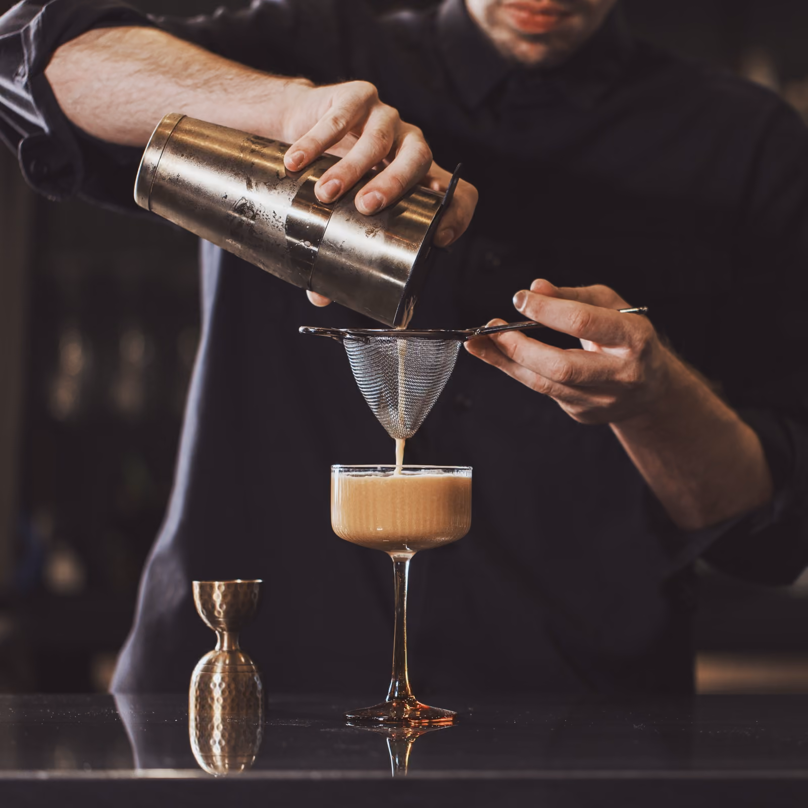 A bartender straining an espresso cocktail into a coupe glass