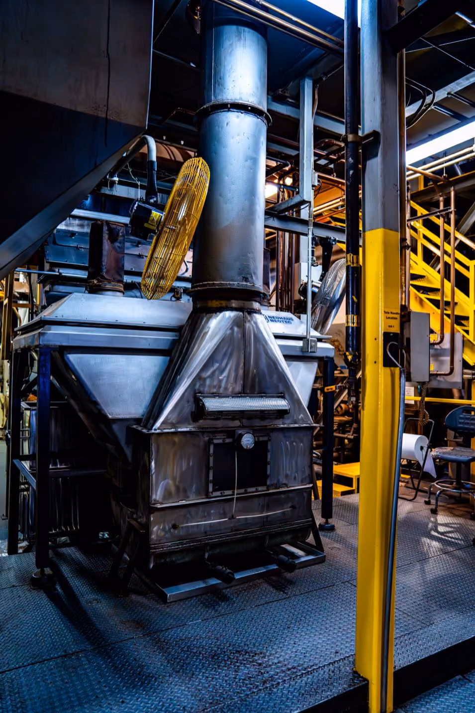 A drum roaster discharging fresh-roasted coffee beans into its cooling tray in a brick-walled roastery