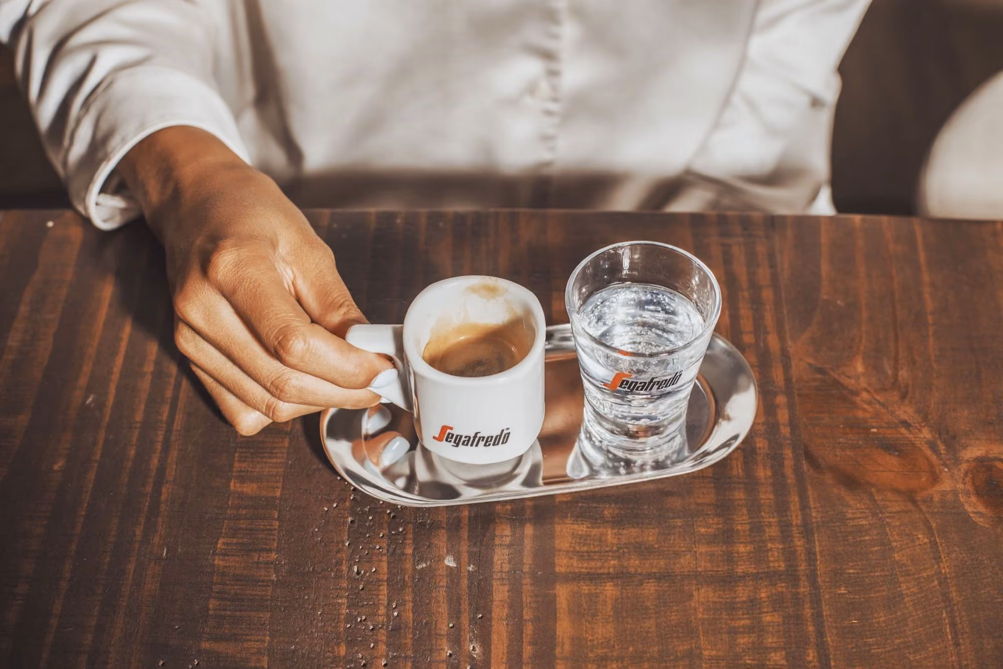 A Segafredo espresso served with a glass of water on a stainless steel tray