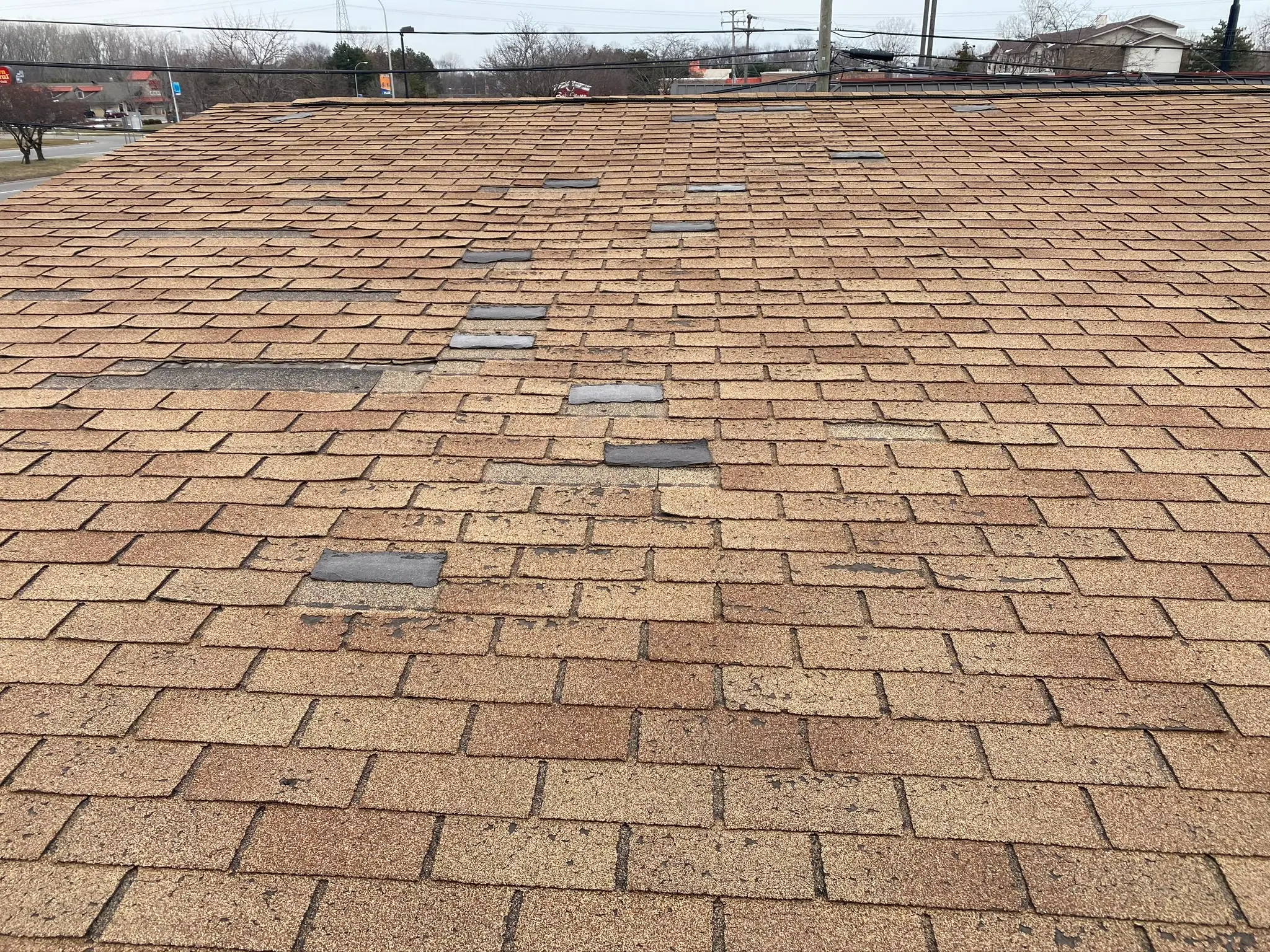 Existing asphalt roof showing multiple localized shingle repairs and material differences