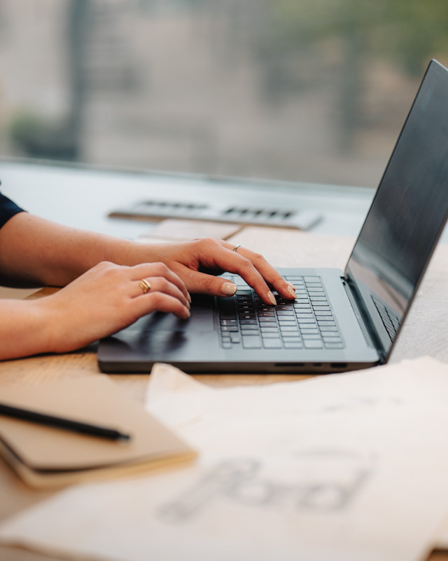 Hands typing on a laptop next to pencil sketches of a logo