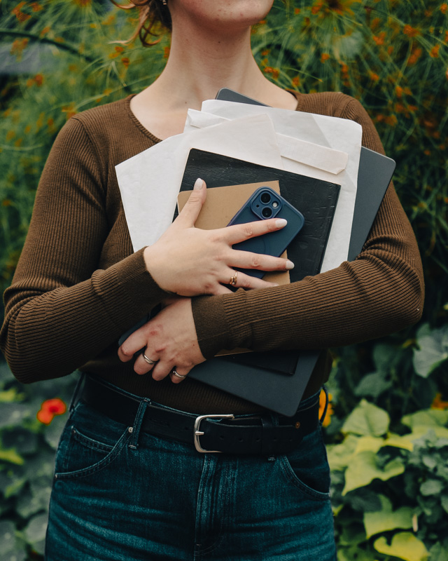 Ellen Bestland holding an armful of folders, a notebook, a laptop and a phone in a garden