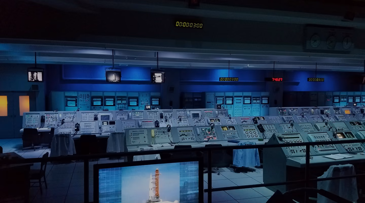 Industrial control room with multiple operator consoles, monitoring screens, and control panels for process operations.