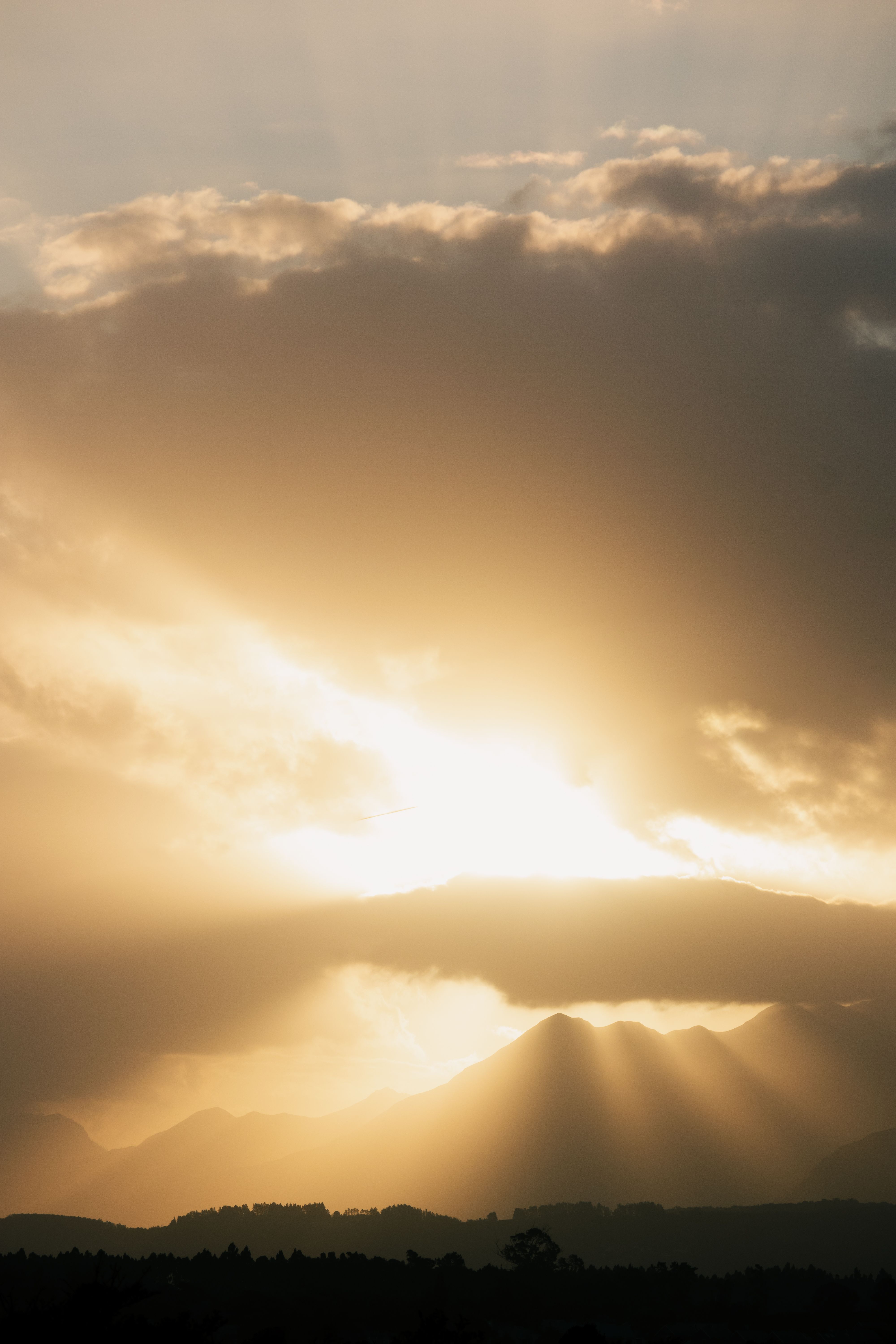 Golden sunbeams breaking through clouds over a mountain silhouette