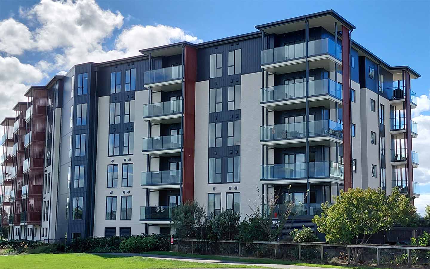 Modern multi-story apartment building with glass balconies under a partly cloudy blue sky.