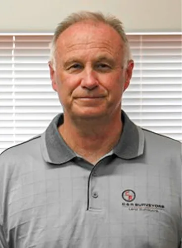 Portrait of a middle-aged man wearing a gray polo shirt with a company logo, standing indoors.
