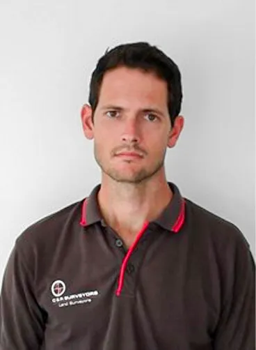 Serious young man with dark hair wearing a brown shirt with red trim against a white background.