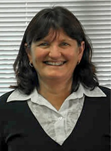 Smiling woman with dark hair wearing a black top over a white collared shirt in front of blinds.