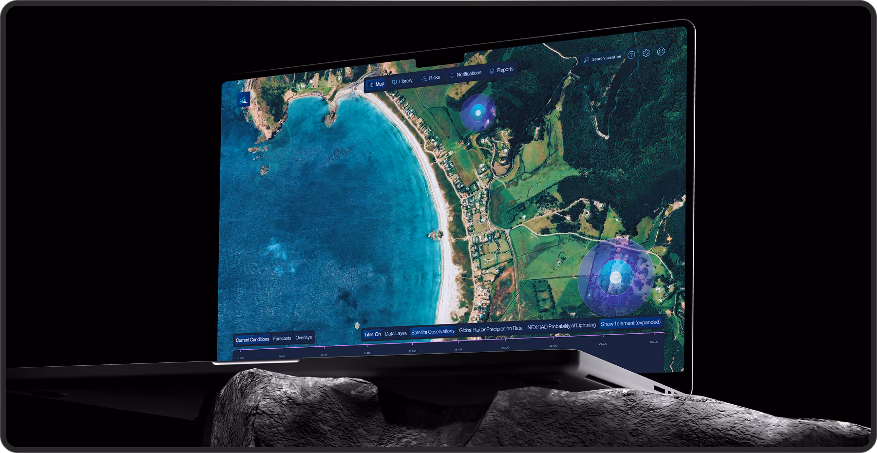 Laptop displaying a satellite map of a coastal area with blue ocean water, a beach, green fields, and forest, showing data layers and overlays related to weather and lightning probability.