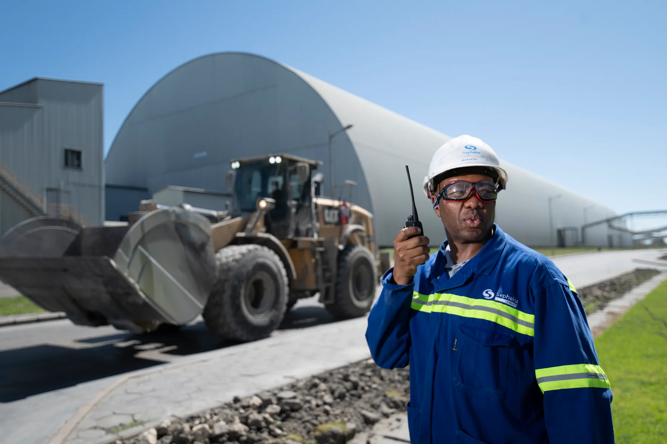Sephaku employee with a two-way radio beside a front-end loader at the Aganang plant