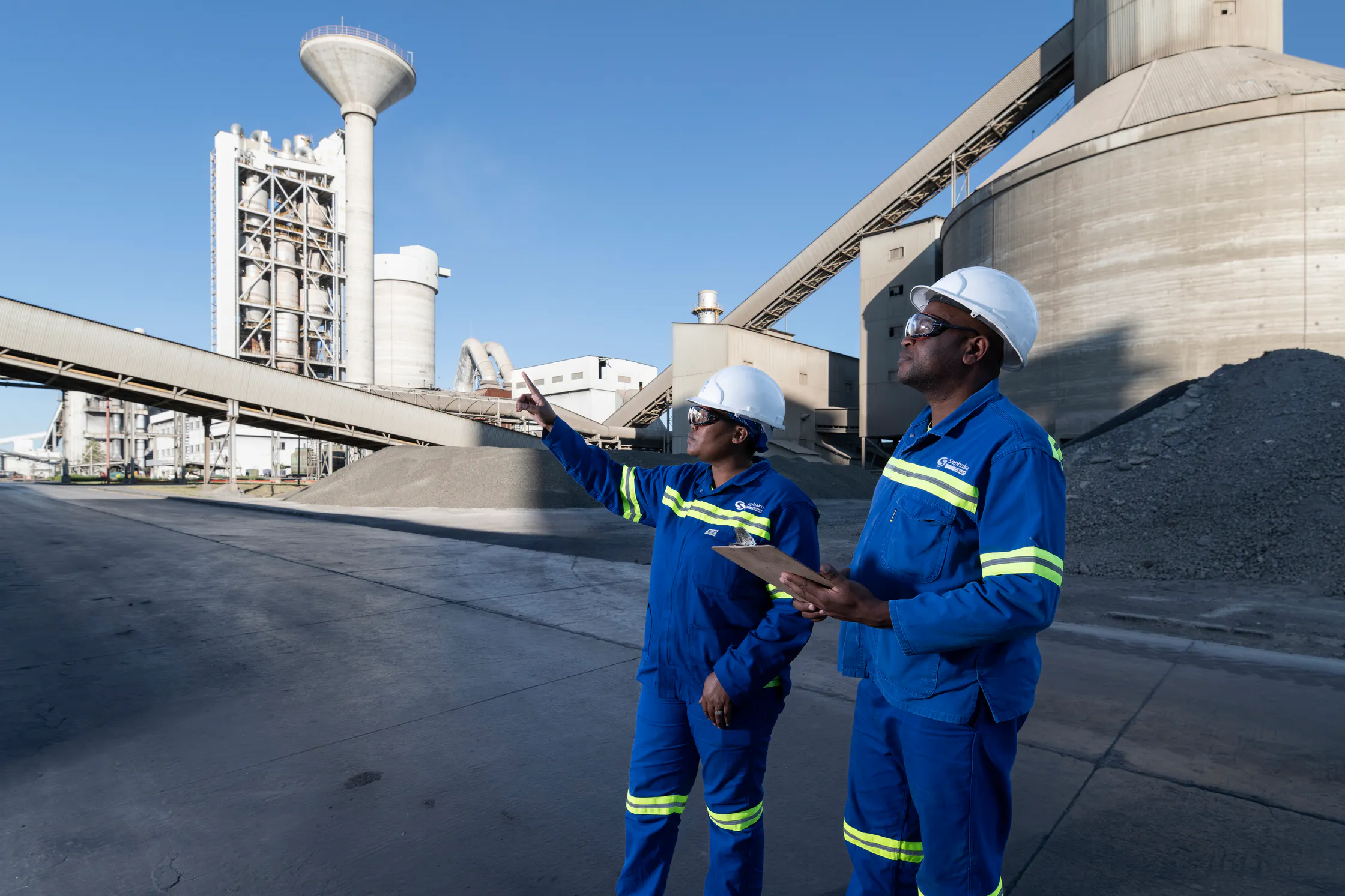 Two Sephaku employees inspecting the Aganang plant beside its storage silos