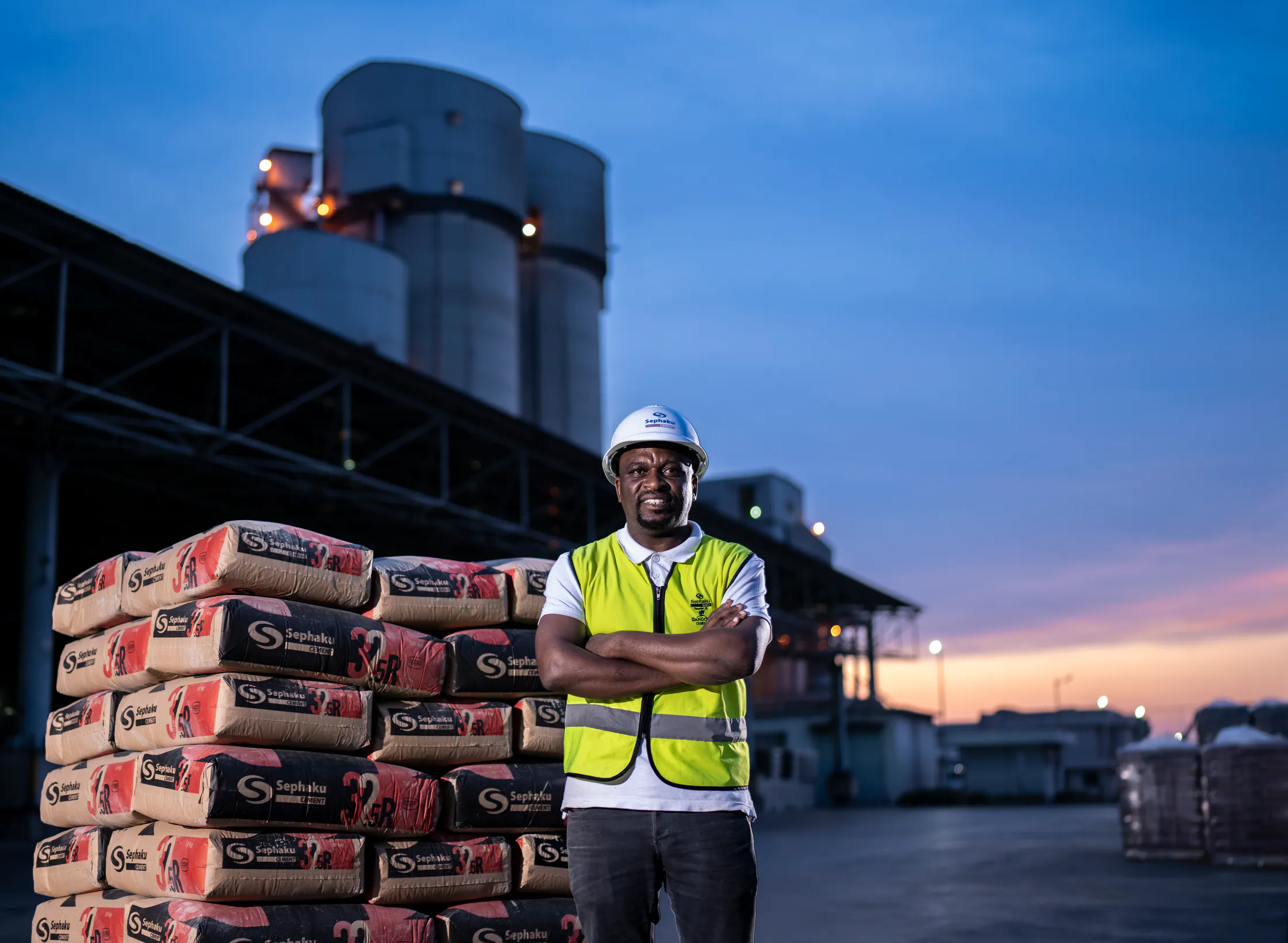 Sephaku employee standing beside stacked cement bags at the Delmas plant at dusk