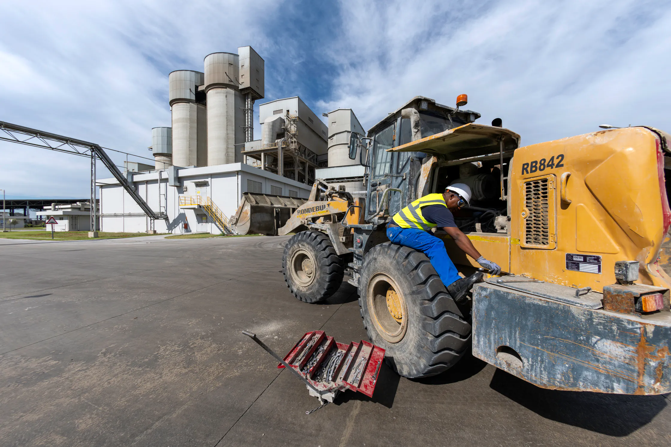 Worker operating a front-end loader in front of the Delmas cement silos