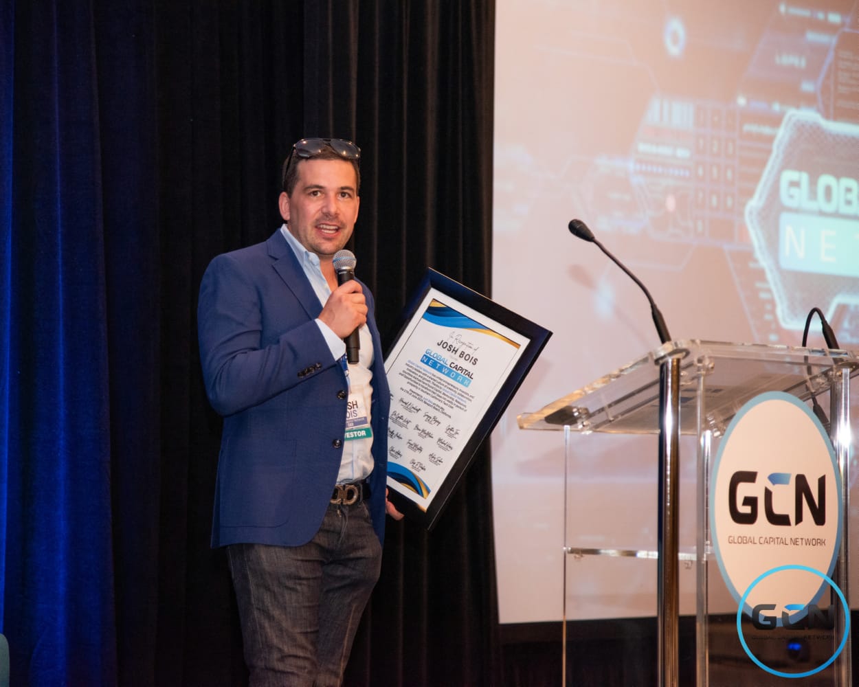 Josh Bois speaking on stage holding the framed recognition award