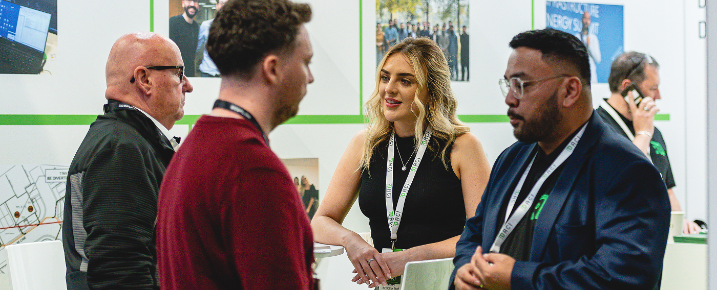 Four people wearing lanyards engaged in conversation at a professional event booth.