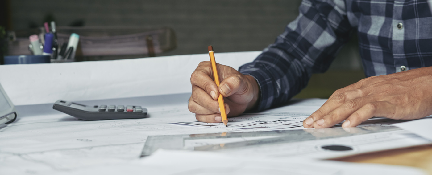 Hands sketching architectural plans with pencil and ruler on a desk with calculator nearby.