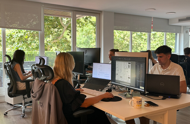 Group of six people having a collaborative discussion around a table in a bright office.