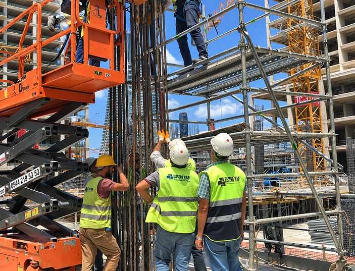 Construction workers in safety gear working on scaffolding and lifting equipment at a building site.