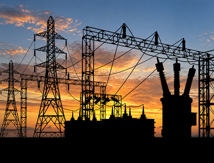 Silhouetted electrical transmission towers and power lines against a colorful sunset sky.