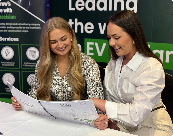 Two DACI team members reviewing engineering plans at an EV infrastructure event stand.