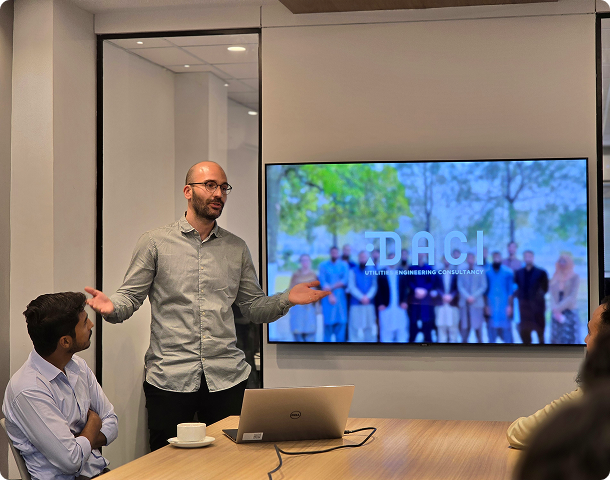 DACI team member presenting to colleagues in a meeting room with a large display screen.