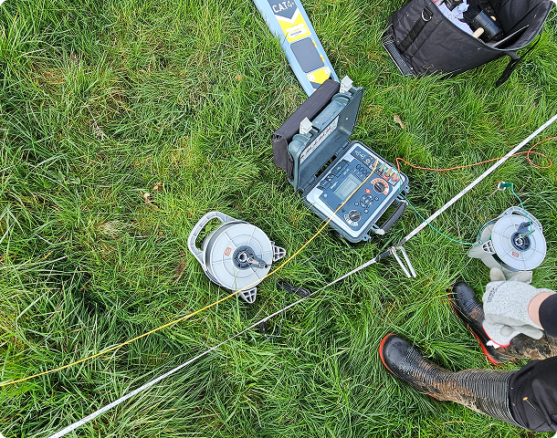 Earth resistance testing equipment and cable reels laid out on grass during a site survey.