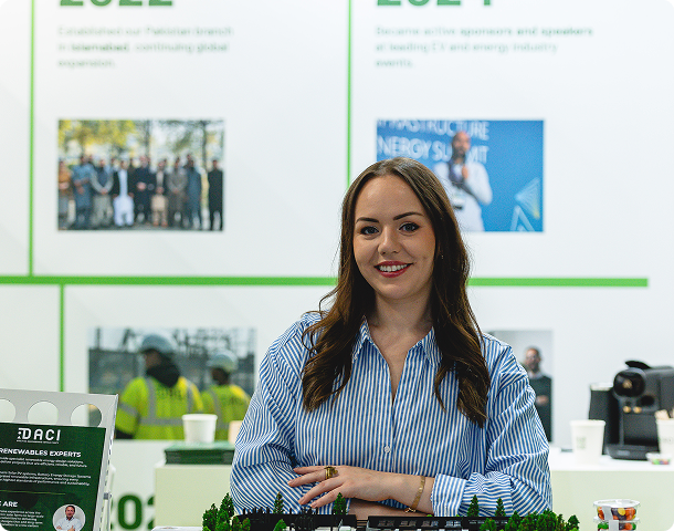 DACI team member smiling at the company exhibition stand with a project milestones display behind her.