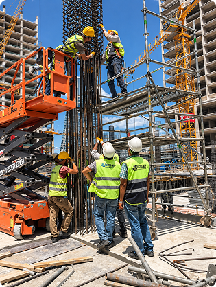 Construction workers in hi-vis vests and hard hats working on scaffolding beside an orange access lift.