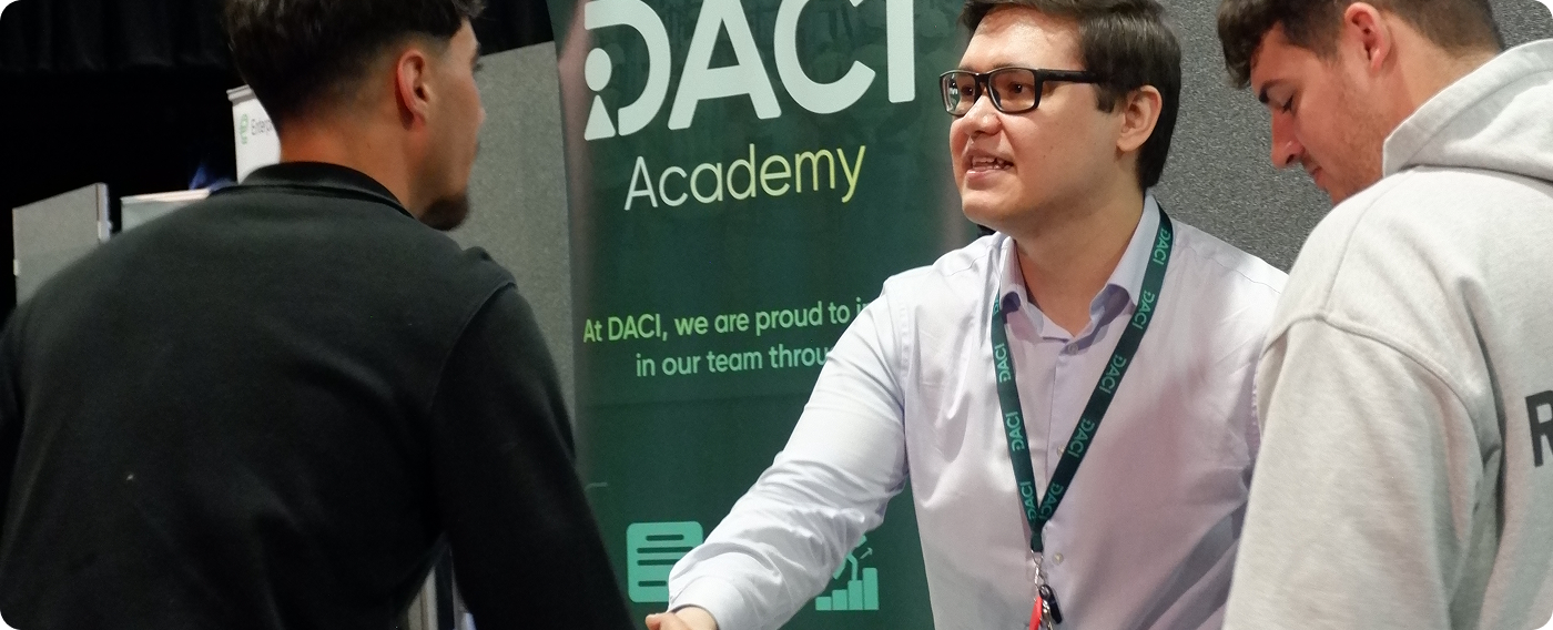 DACI engineer talking with visitors at the DACI Academy stand during an industry event.