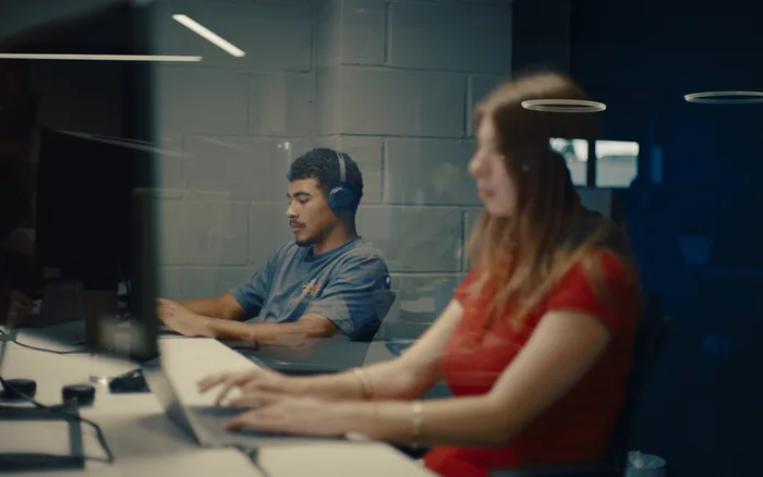Two Halo colleagues working at adjacent desks, one wearing headphones