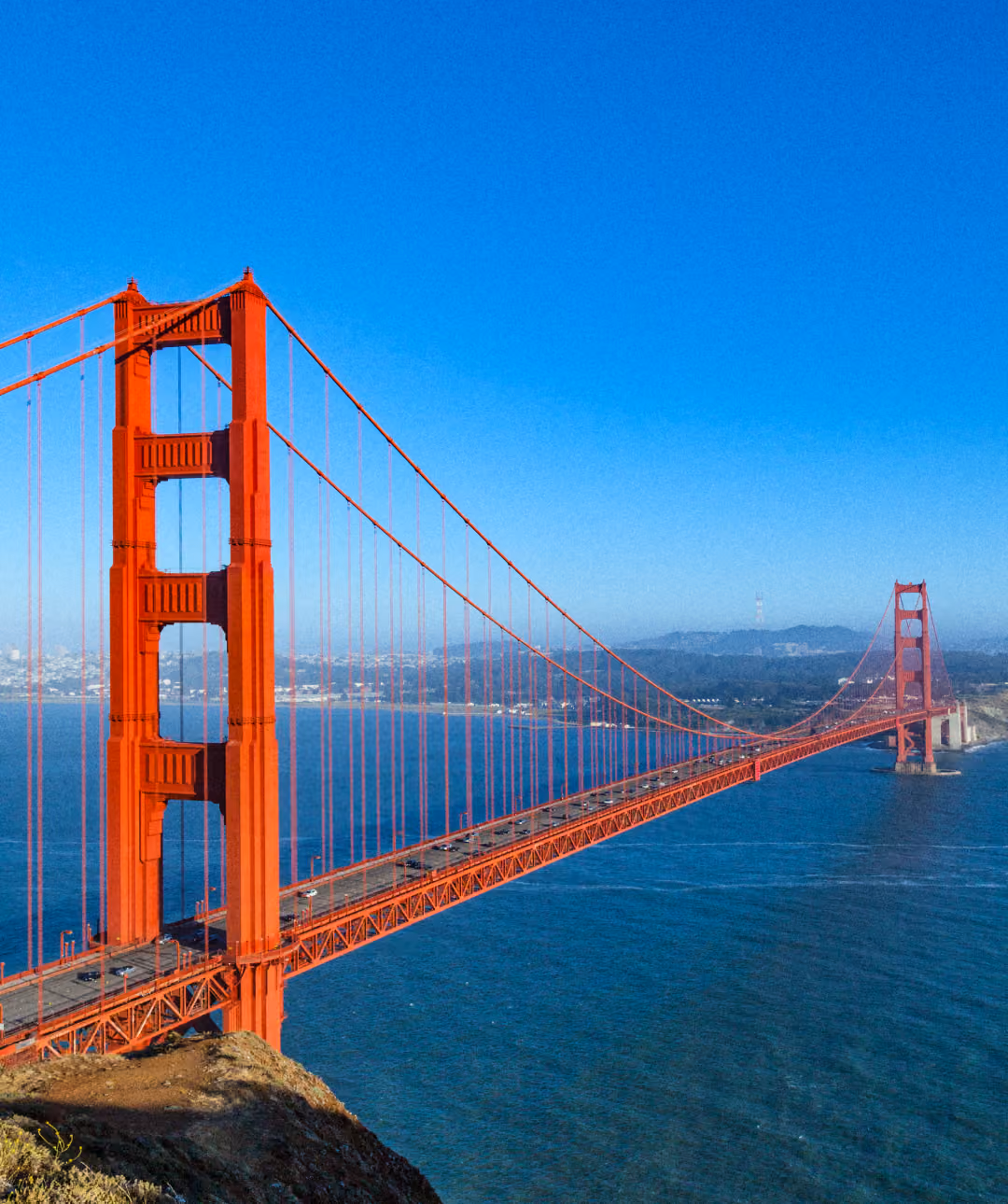 High-angle view of the red Golden Gate Bridge stretching across blue water under a clear blue sky.