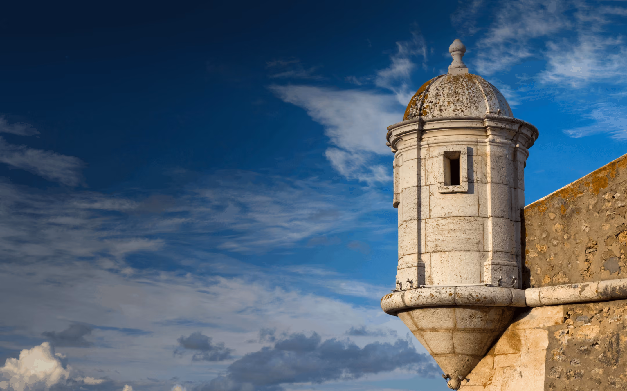 Historic stone watchtower on a fortress wall against a blue sky with clouds.