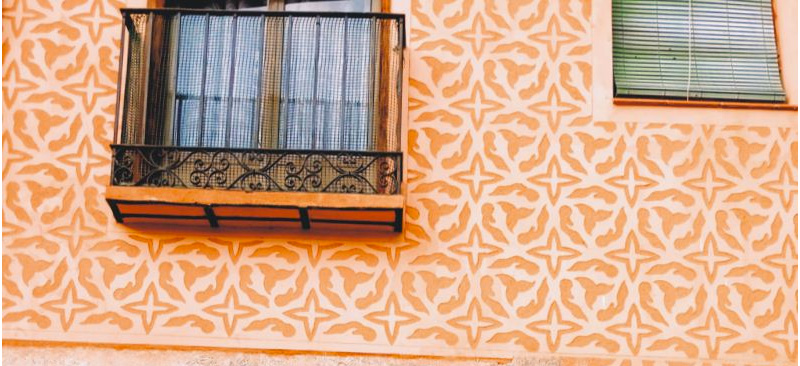 A window with a small balcony with orange wall decorated with a repeating geometric pattern