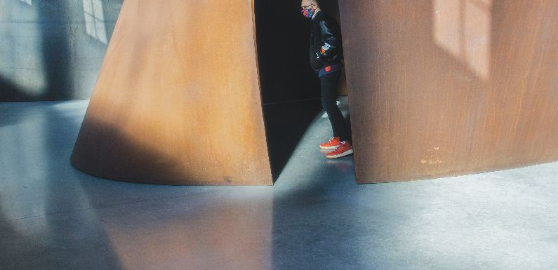 Person wearing a face mask and red shoes standing between two large structures on a polished cement floor