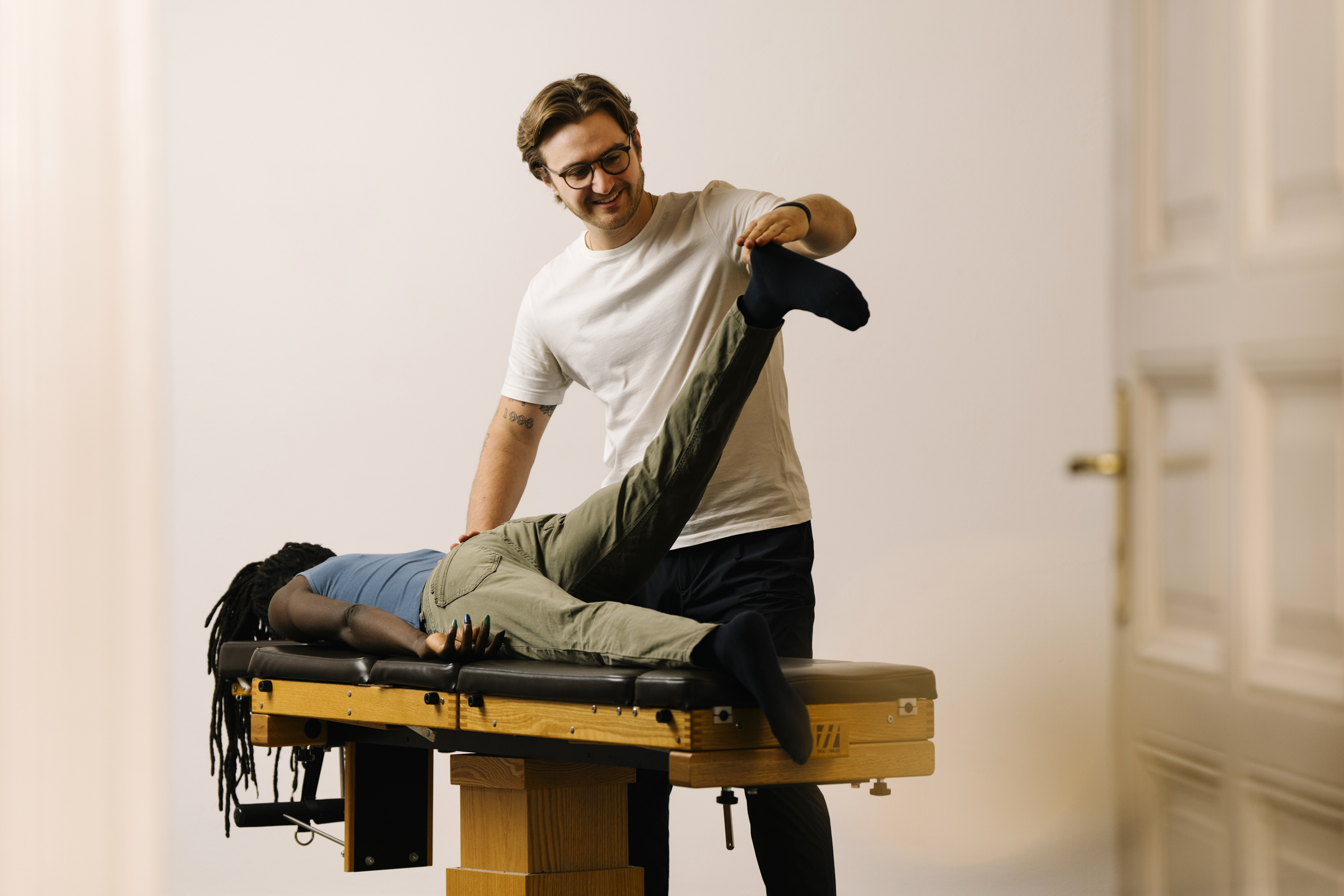 Chiropraktiker Max prüft bei einer liegenden Patientin die Beinlänge, um eine mögliche Hüftjustierung vorzubereiten.