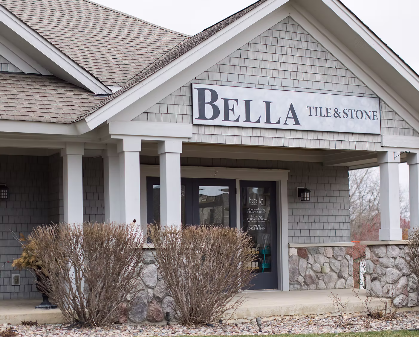 Bella Tile and Stone storefront with shingle siding, white columns, and stone base.