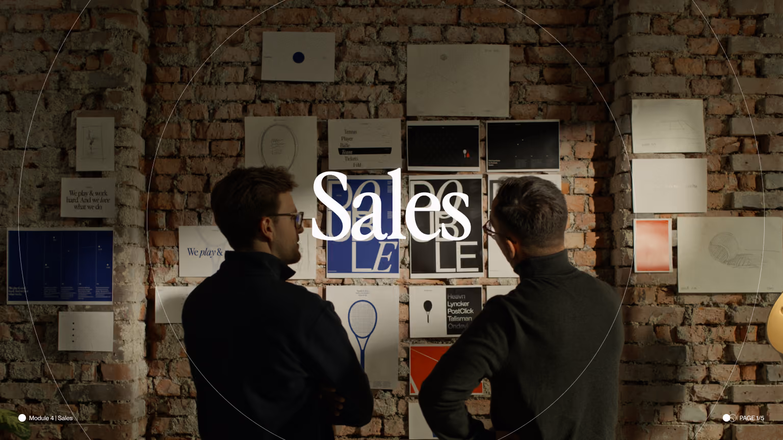 Two men in black sweaters looking at designs pinned on a brick wall in a creative workspace.