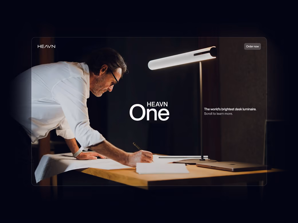Man writing at a desk illuminated by a modern HEAVN One desk lamp in a dark room.
