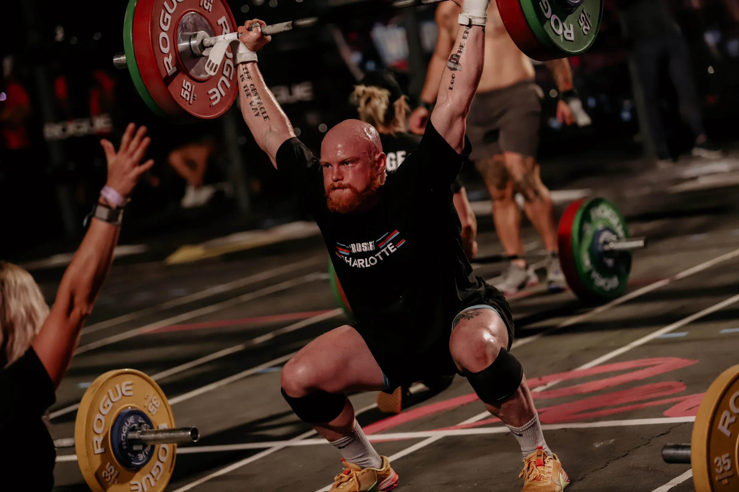 Taylor holding a barbell locked out overhead at the bottom of an overhead squat under competition lights.