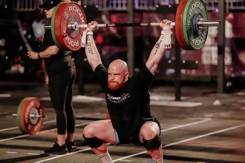 Taylor catching a loaded barbell overhead in a deep squat during a competition.