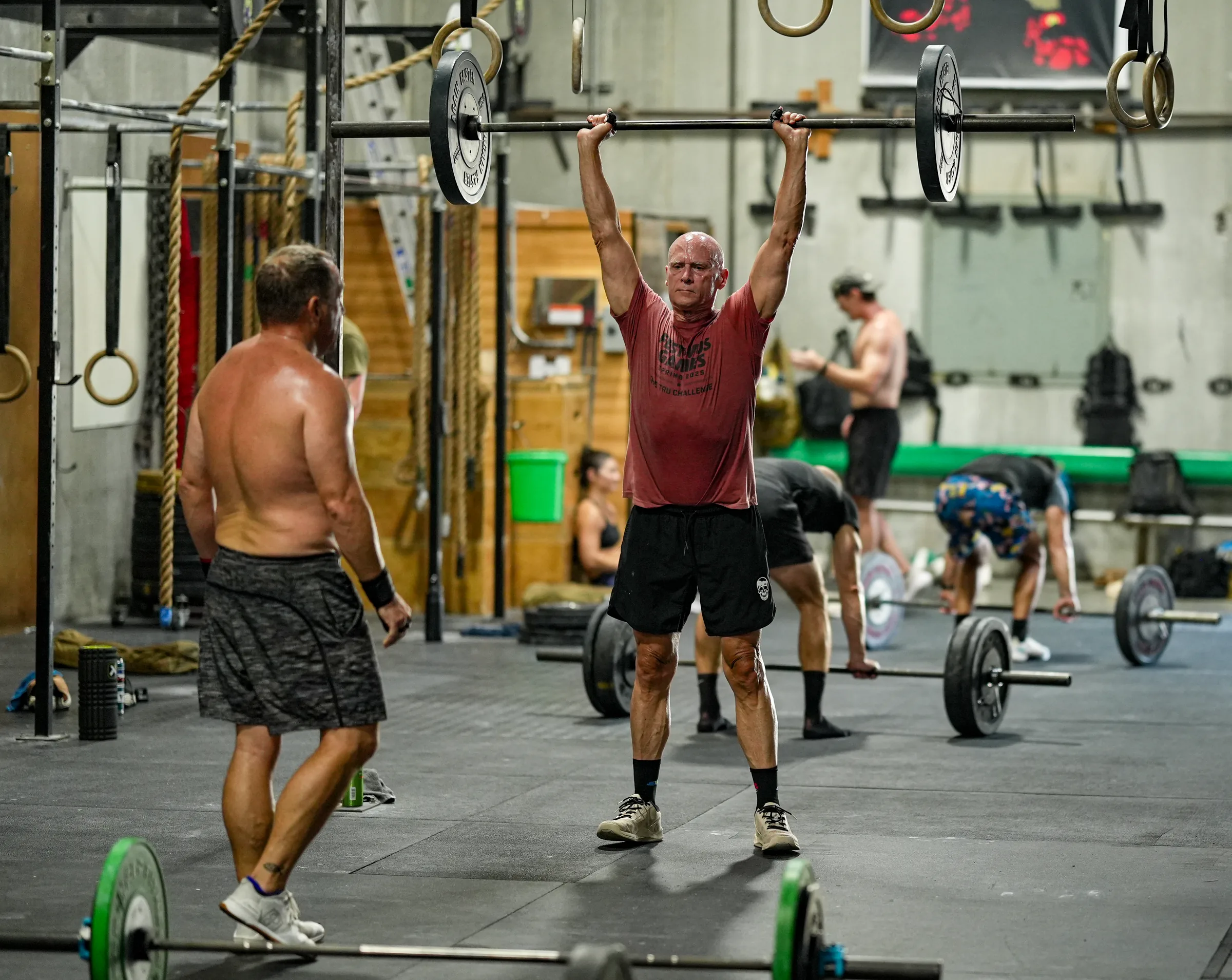 A class of athletes holding barbells overhead in the gym.