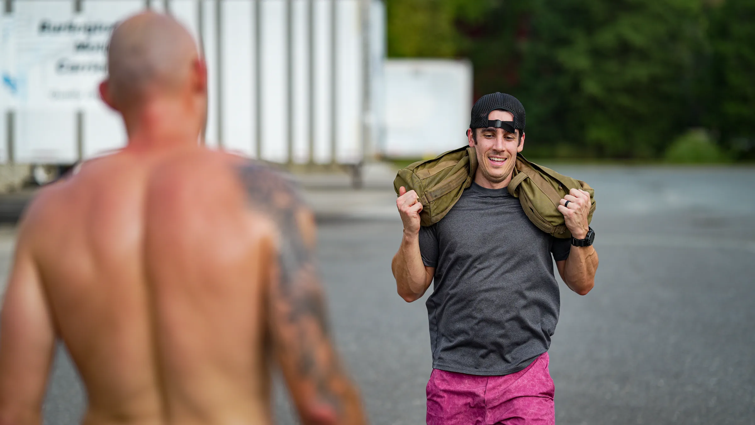 An athlete carrying a sandbag on his shoulders during an outdoor class workout.